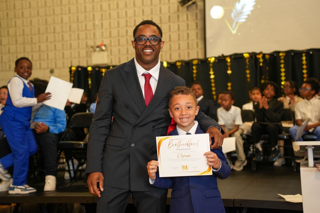A young man beams while holding up his certificate.
