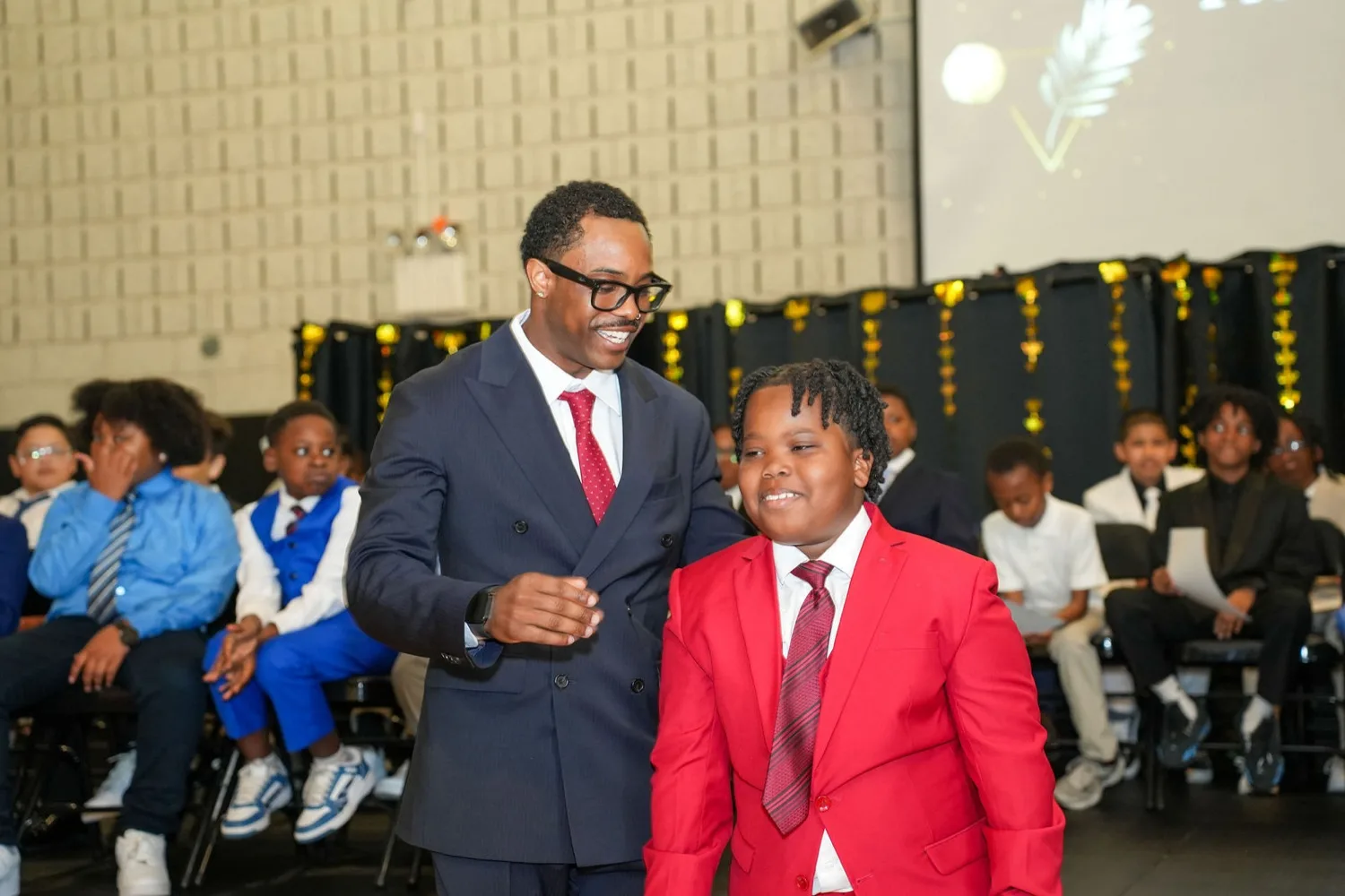 Founder Kale Blackshear laughing with a young man in a red suit at the induction ceremony.
