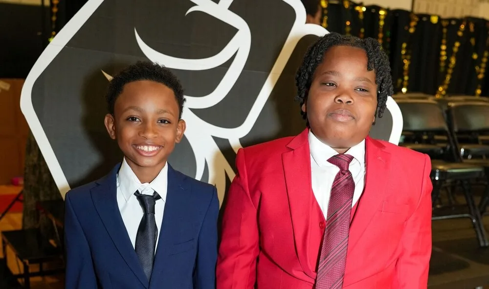 Two young inductees in their suits in front of the Brotherhood fist banner.