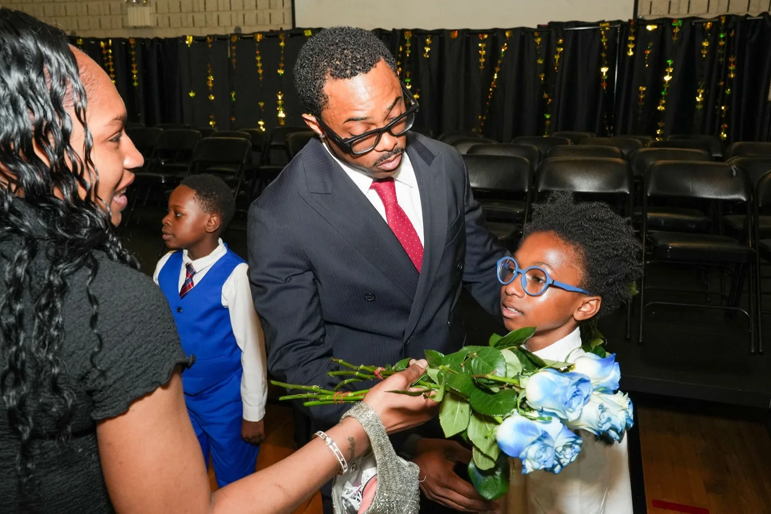 A mentor and a young man holding blue roses with a proud family member after the induction ceremony.